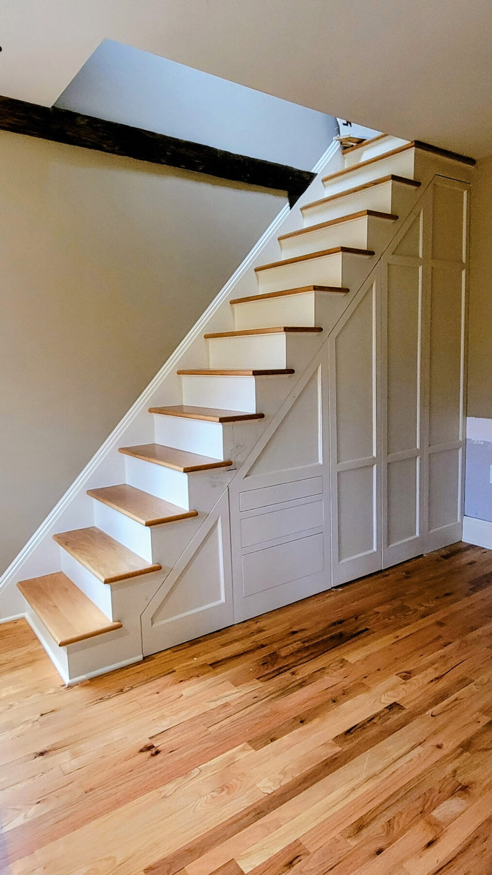 Custom under-stair storage with concealed paneled doors and built-in cabinetry shown closed in Connecticut