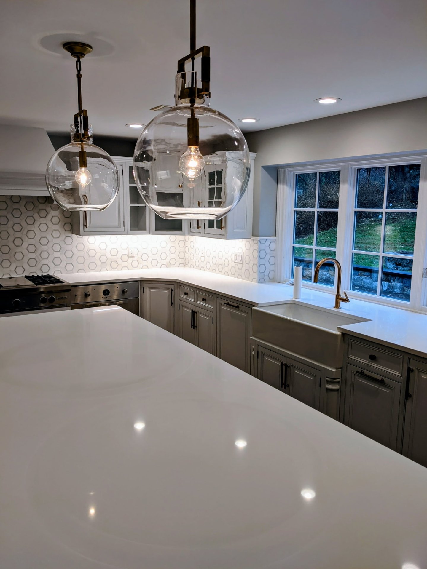 White glass-front upper cabinets and gray base cabinetry surrounding a farmhouse sink in Ridgefield, CT.