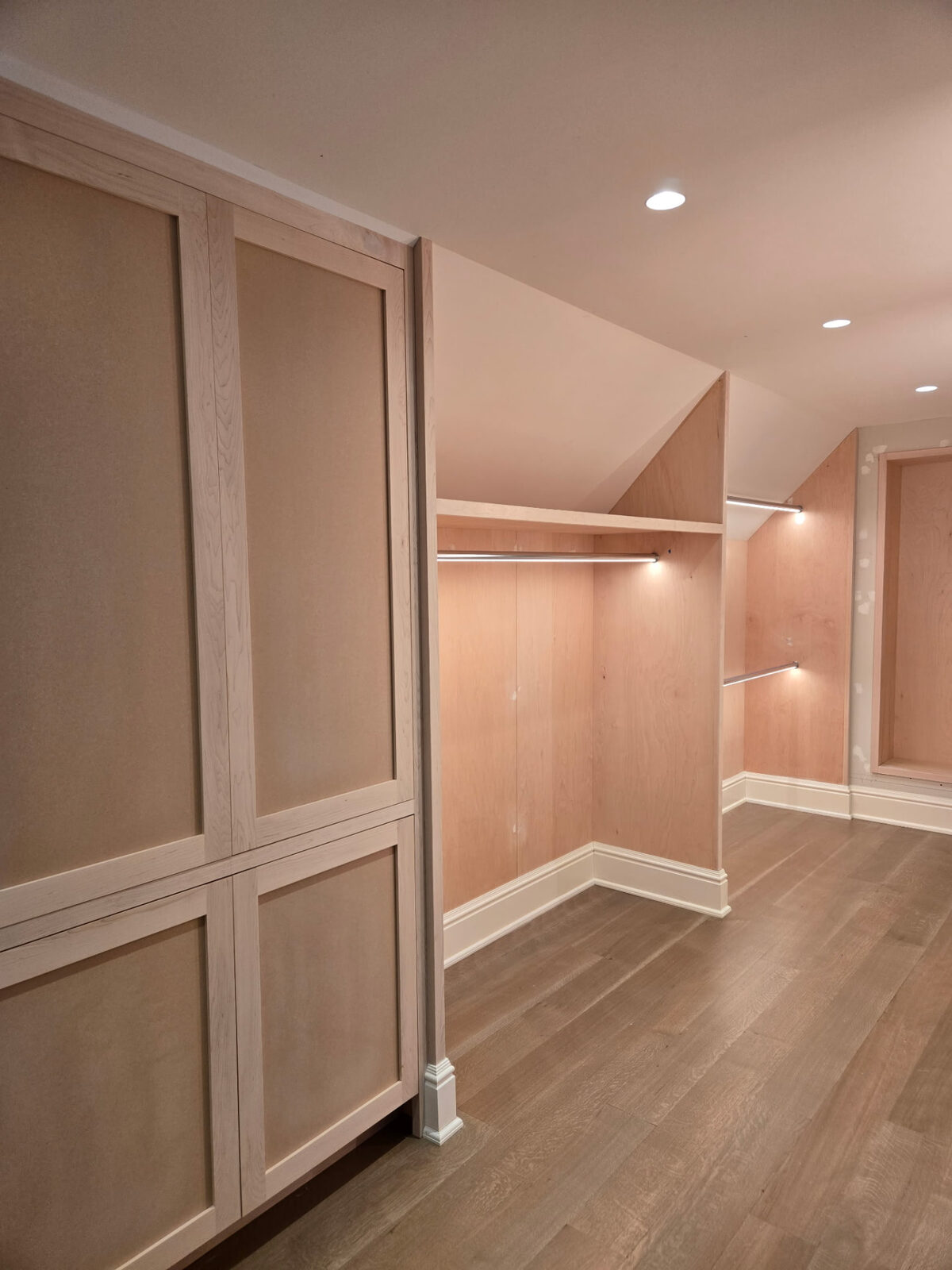 Custom walk-in closet cabinetry installation in Ridgefield Connecticut, showing unfinished wood cabinetry and integrated lighting