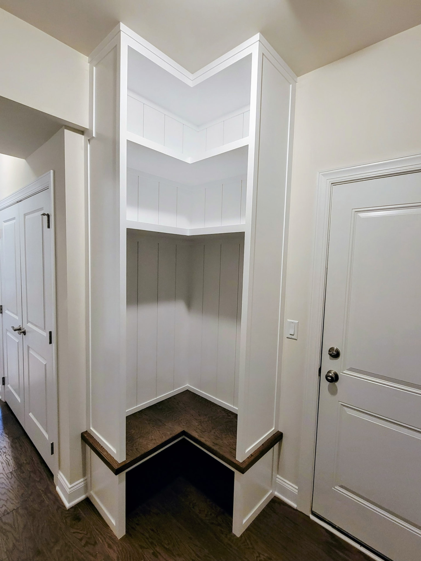 Custom white mudroom built-in with corner shelving and dark wood bench in Ridgefield CT by Glissmann Construction