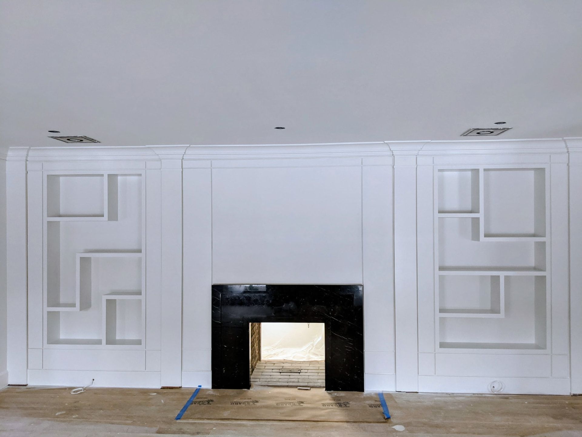 Painted white asymmetric built-in shelving and wall paneling around a fireplace, straight-on view, in Greenwich CT