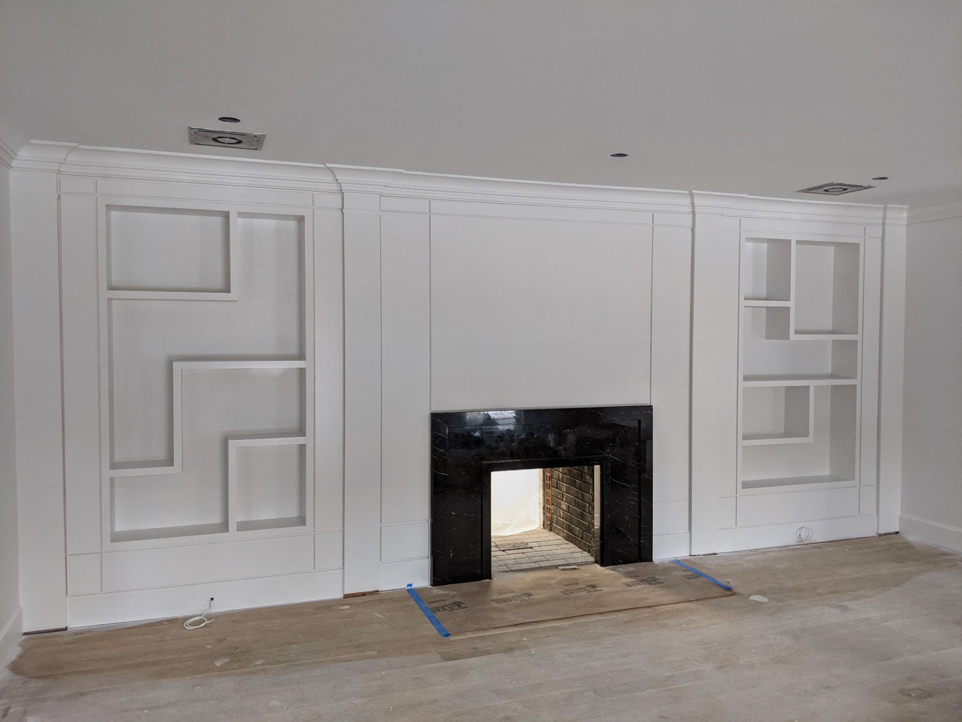 Painted white asymmetric built-in shelving and black marble fireplace seen at an angle, in Greenwich CT