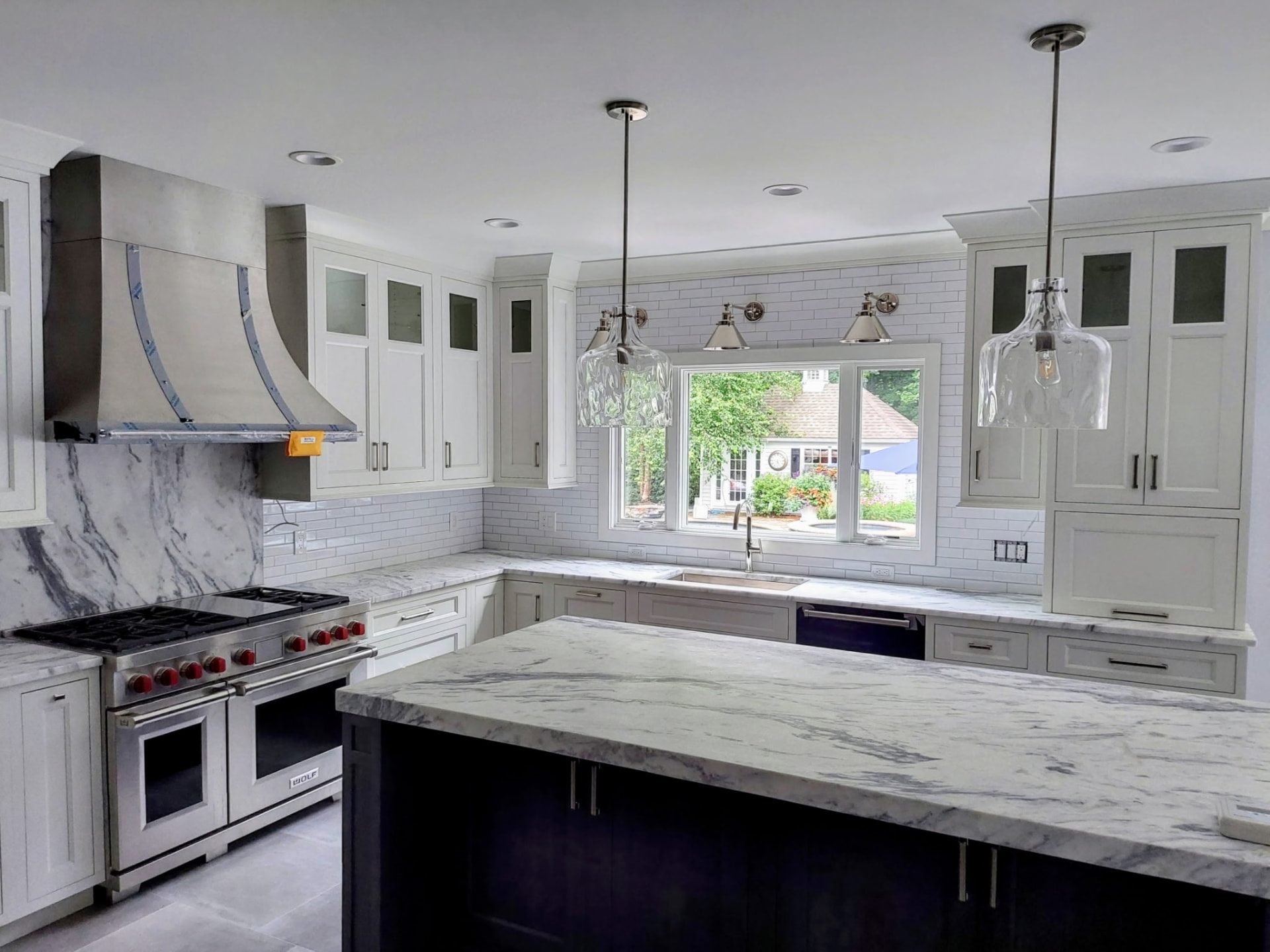 Light-colored kitchen cabinetry with glass-front upper doors and a dark island in Westchester County, NY.