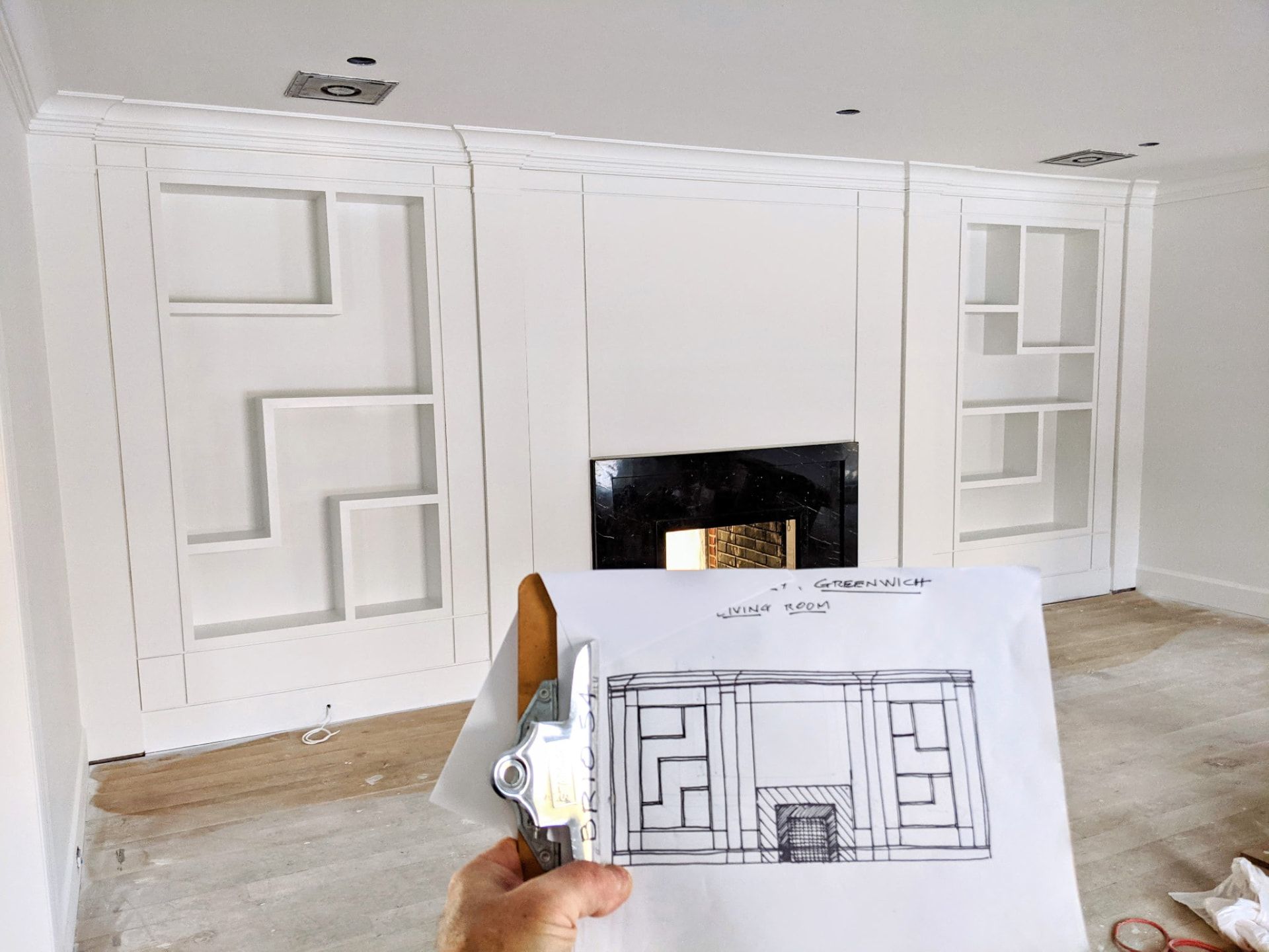 Design drawing for a Greenwich CT living room held up in front of the installed asymmetric built-in shelving and fireplace