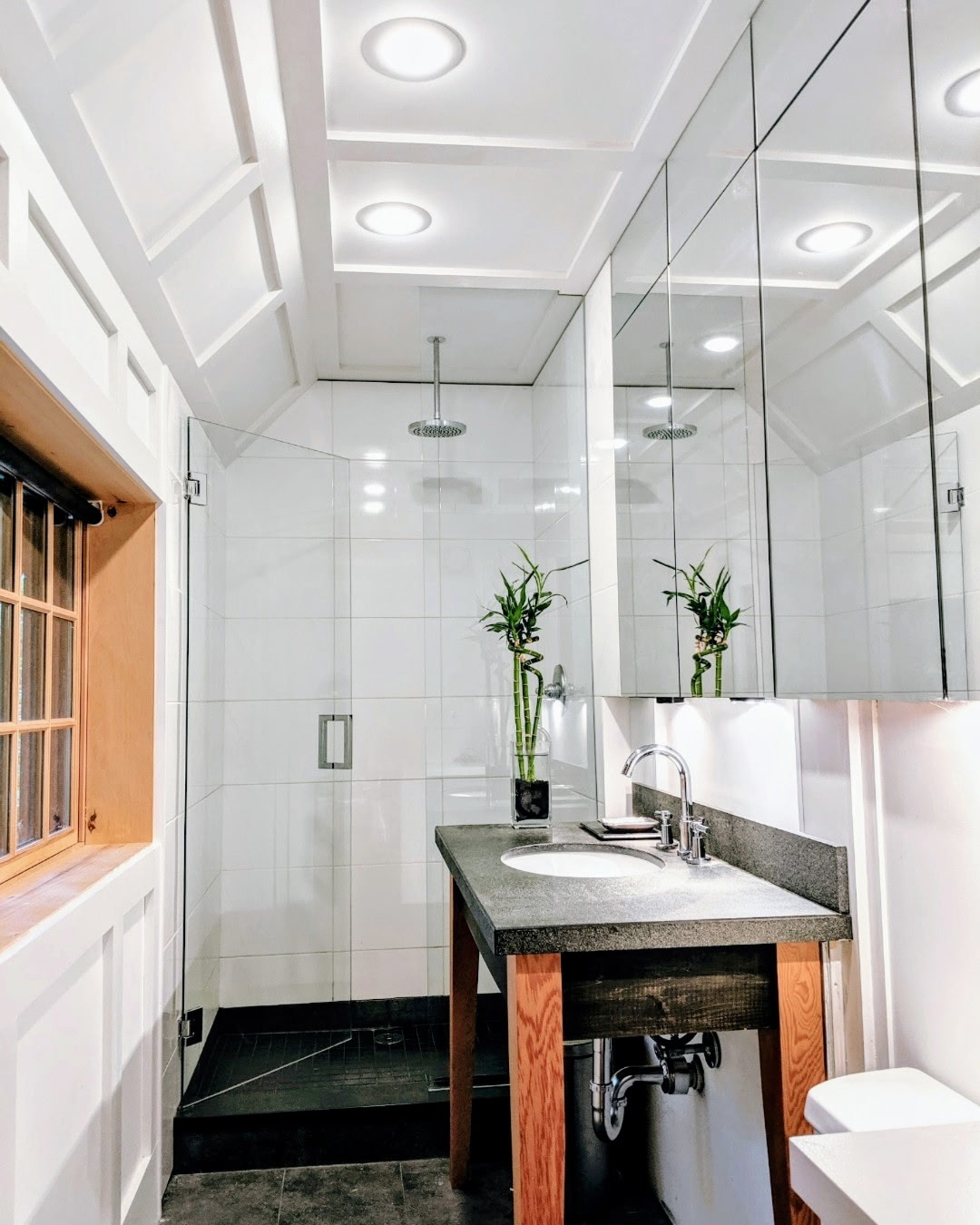 Custom bathroom in Ridgefield CT by Glissmann Construction — glass-enclosed walk-in shower, mirrored cabinetry, and a wood vanity with stone countertop