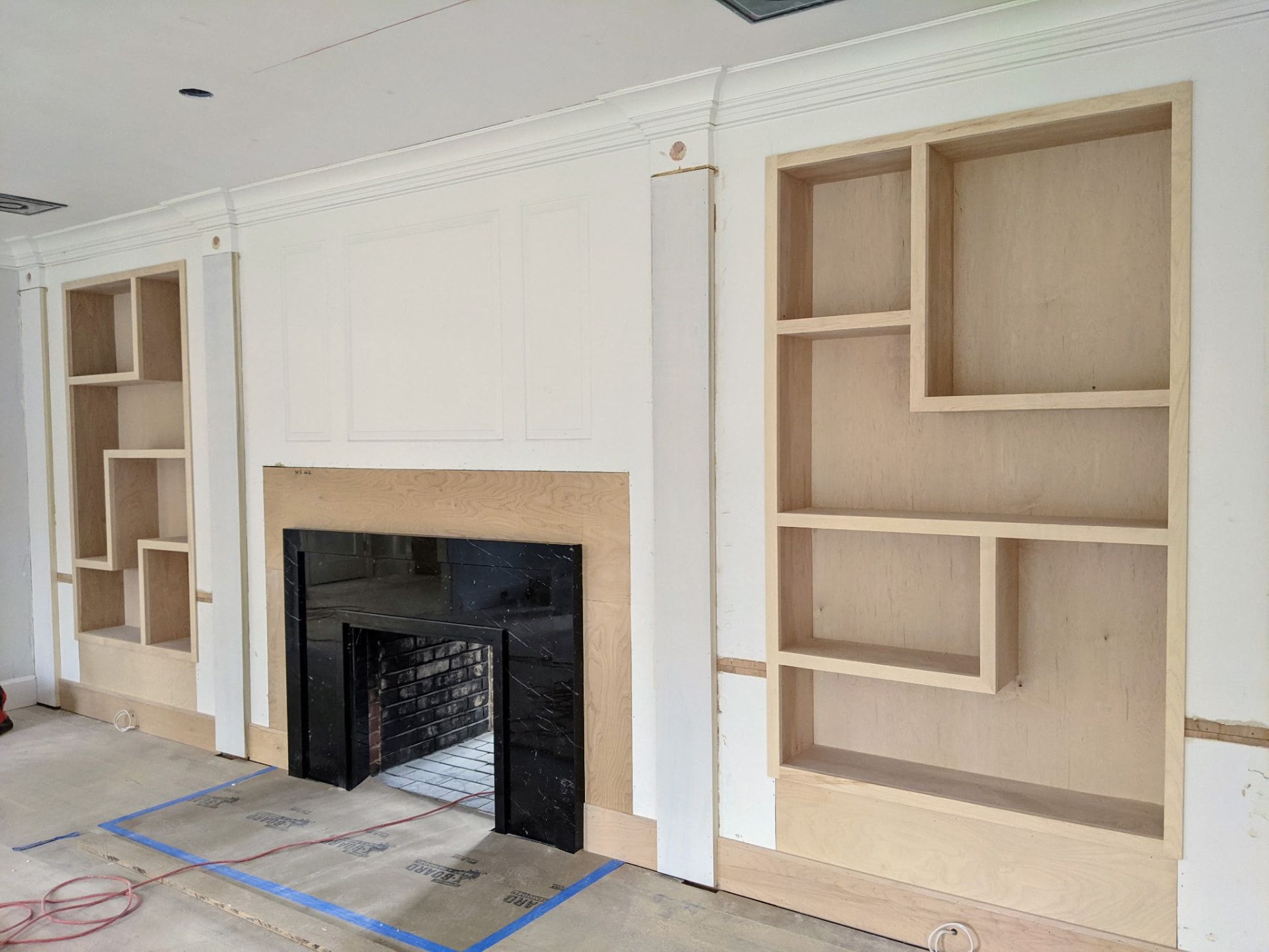 Unfinished asymmetric built-in shelving in raw plywood, angled view showing the depth of the right-hand unit, in Greenwich CT